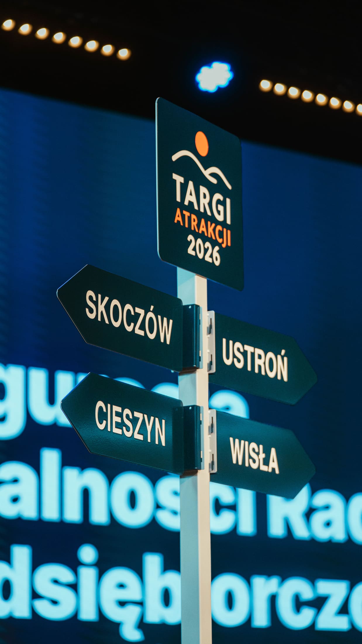 Drogowskaz z logo Targów Atrakcji 2026 i tabliczkami Skoczów, Ustroń, Cieszyn i Wisła na scenie w Konfero