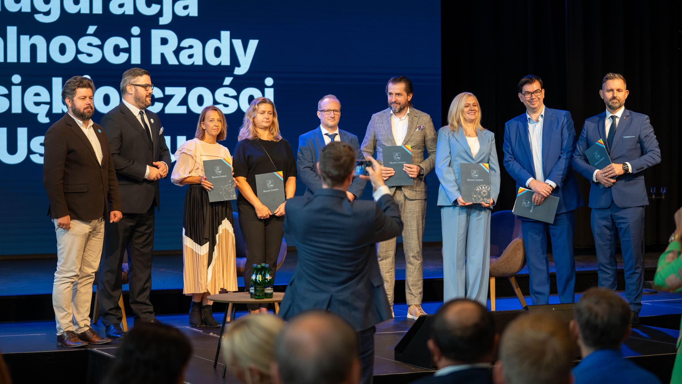 Cała nowo powołana Rada Przedsiębiorczości Miasta Ustroń pozuje na scenie z folderami Miasta Ustroń